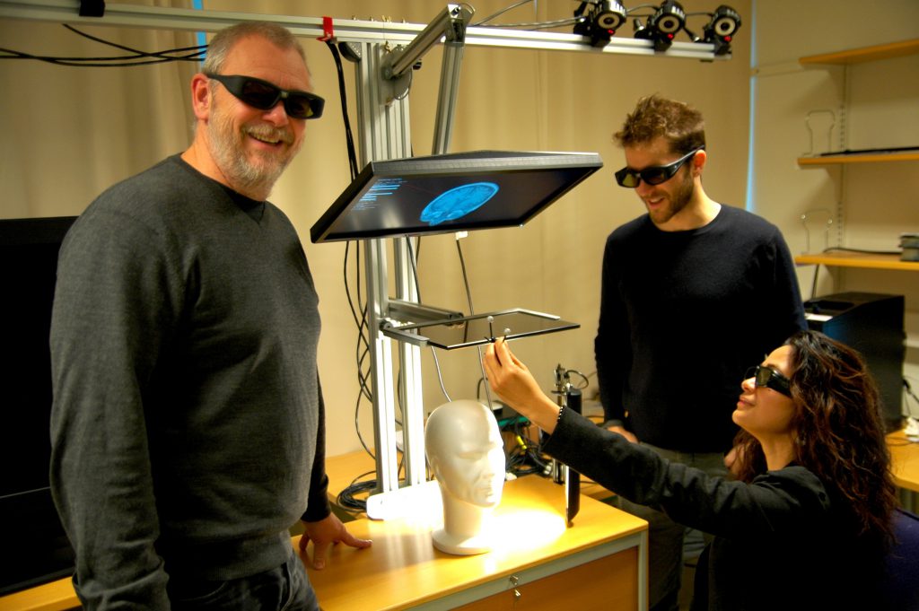 Three researchers wearing 3D glasses around a stereoscopic display rig in the Sense-IT lab